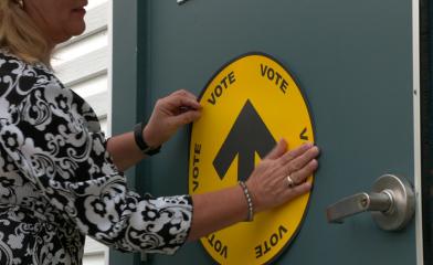 A women posting a sign on a door that says "Vote".