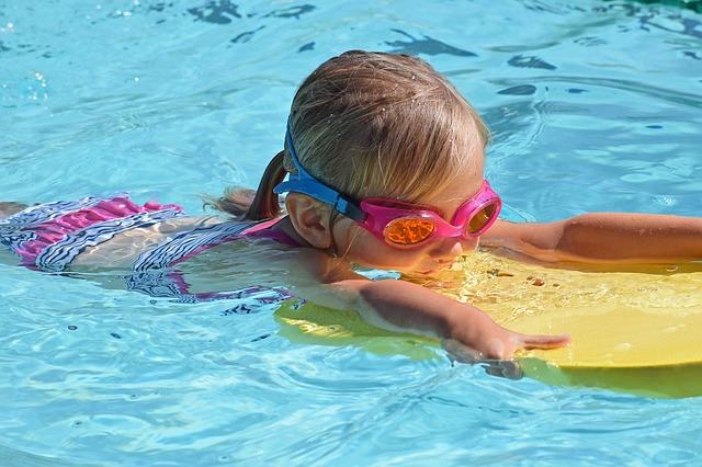 Child swimming on flutterboard in a pool. Child is wearing goggles. 