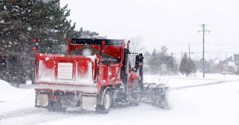 A red Town snow plow clearing a snow-covered street.